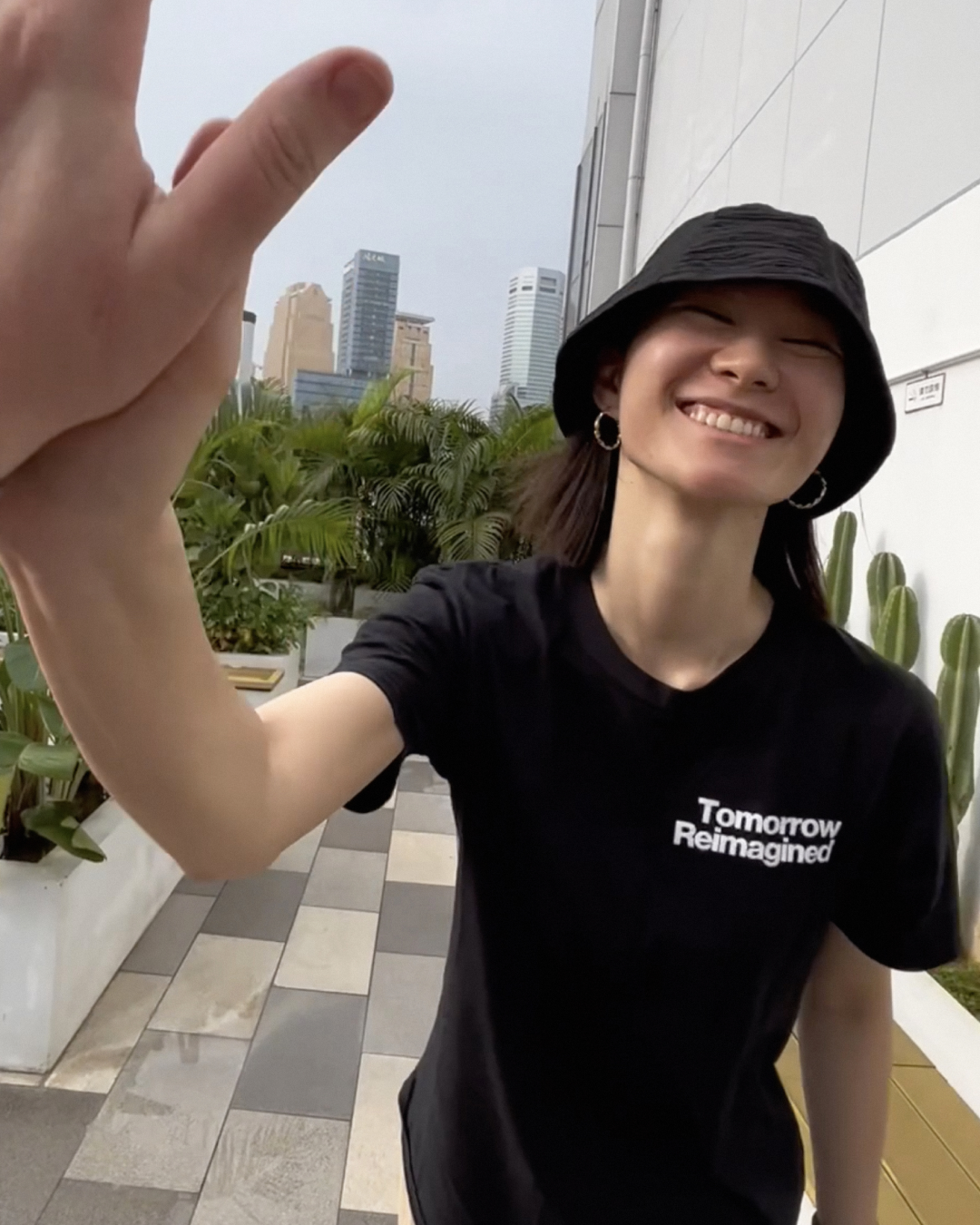 ZURU team member standing outside smiling to camera, wearing black bucket hat and black "Tomorrow Reimagined" t-shirt