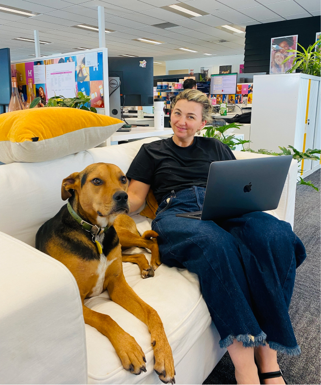 Person sitting on couch with their laptop in an office next to a friendly dog