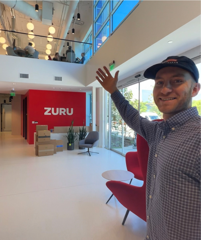 Person showing viewer around ZURU office, red ZURU logo wall in background